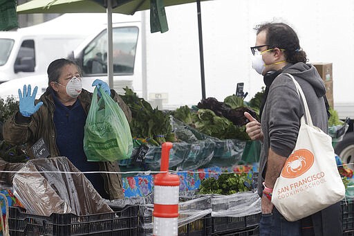 Annabelle Lenderink, left, wears a mask while helping customer Justin Angel at the Star Route Farms stand at the Ferry Plaza Farmers Market in San Francisco, Saturday, March 28, 2020. (AP Photo/Jeff Chiu)