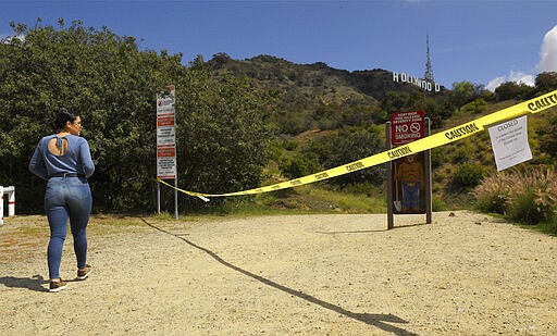 Tourist Paola Cornejo stands at the entrance to Innsdale Trail that has been closed off near the Hollywood Sign, Saturday, March 28, 2020, in Los Angeles. With cases of coronavirus surging and the death toll surpassing 100, lawmakers are pleading with cooped-up Californians to spend a second weekend at home to slow the spread of the infections. (AP Photo/Mark J. Terrill)