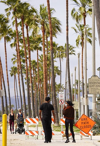 Pedestrians walk along a closed Venice Beach boardwalk, Saturday, March 28, 2020, in Los Angeles. With cases of coronavirus surging and the death toll surpassing 100, lawmakers are pleading with cooped-up Californians to spend a second weekend at home to slow the spread of infections. (AP Photo/Mark J. Terrill)