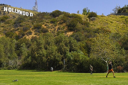 Two men play catch at Lake Hollywood Park near the famed Hollywood Sign, Saturday, March 28, 2020, in Los Angeles. With cases of coronavirus surging and the death toll surpassing 100, lawmakers are pleading with cooped-up Californians to spend a second weekend at home to slow the spread of the infections. It has been more than a week since Gov. Gavin Newsom barred 40 million residents from going outdoors except for essentials. Even so, reports of crowds have prompted local and state officials to warn that ignoring social distancing, park and beach closures could spread the virus, which already is surging. (AP Photo/Mark J. Terrill)