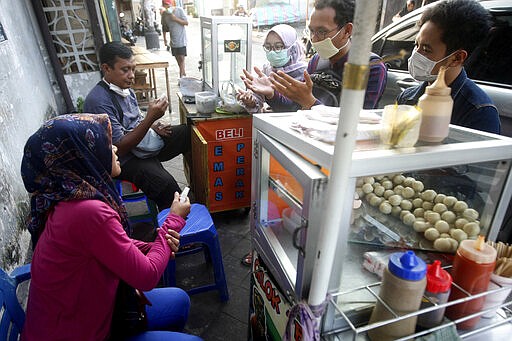 In this Thursday, March 26, 2020 photo, activists explain how to use hand sanitizers and soaps to street food vendors in Yogyakarta, Indonesia. A group of students from several universities in the central Java city has distributed soaps and hand sanitizers to informal daily workers whose incomes are affected by the coronavirus outbreak. (AP Photo/Fahmi Rosyidi)