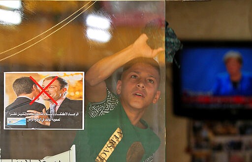 File - In this Thursday, March 19, 2020 file photo, a young worker cleans the window of a barbershop that posts a warning sign referring to the coronavirus, with Arabic that reads, &quot;Please greet only and don't kiss, due to the difficult circumstances in the current situation,&quot; in Baghdad, Iraq. Iraq announced a weeklong curfew to help fight the COVID-19 pandemic. (AP Photo/Hadi Mizban, File)