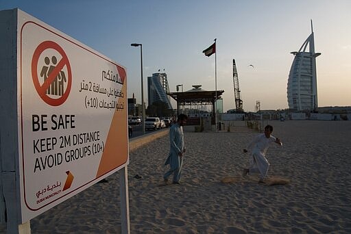 File - In this Friday, March 20, 2020 file photo, two laborers play tag near a sign warning people to maintain a distance from each other over the outbreak of the new coronavirus in front of the sail-shaped Burj Al Arab luxury hotel in Dubai, United Arab Emirates. The United Arab Emirates has closed its borders to foreigners, including those with residency visas, over the coronavirus outbreak, but has yet to shut down public beaches and other locations over the virus. (AP Photo/Jon Gambrell, File)