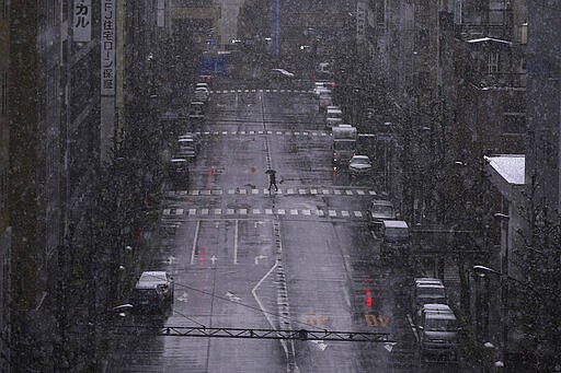 FILE - In this March 29, 2020, file, photo, a person walks in falling snow in Tokyo. Before the Olympics were postponed, Japan looked like it had coronavirus infections contained, even as they spread in neighboring countries. Now that the games have been pushed to next year, Tokyo&#146;s cases are spiking, and the city's governor is requesting that people stay home, even hinting at a possible lockdown.  (AP Photo/Eugene Hoshiko, File)