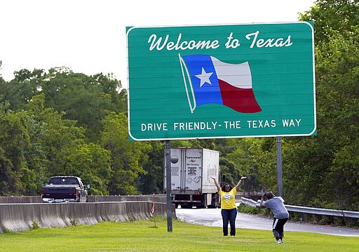 Mia Davis, center, poses as he husband, Gus, takes her picture Sunday, March 29, 2020, at a rest stop along I-10 in Orange, Texas, near the Louisiana border. The couple is moving from Washington D.C. to San Antonio. Texas is ratcheting up restrictions on neighboring Louisiana, one of the growing hot spots for coronavirus in the U.S. Just two days after Texas began requiring airline passengers from New Orleans to comply with a two-week quarantine, Texas Gov. Greg Abbott said state troopers will now also patrol highway entry points at the Louisiana border. (AP Photo/David J. Phillip)