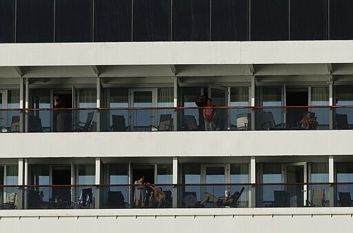 Passengers stand on balconies of the Zaandam cruise ship, anchored in the bay of Panama City, Friday, March 27, 2020. Several passengers have died aboard the cruise ship and a few people aboard the ship have tested positive for the new coronavirus, the cruise line said Friday, with hundreds of passengers unsure how long they will remain at sea. (AP Photo/Arnulfo Franco)