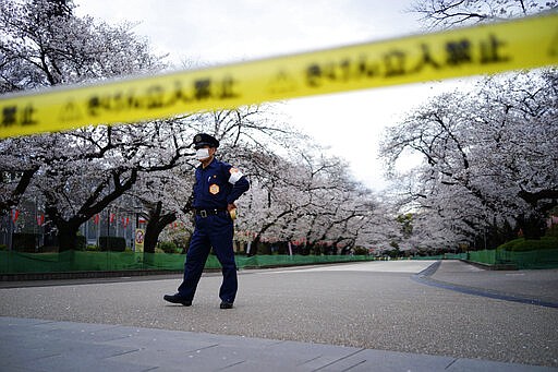 FILE - In this March 27, 2020, file, photo, a security person stands guard at the famed street of cherry blossoms which is closed as a safety precaution against the new coronavirus at Ueno Park in Tokyo. Before the Olympics were postponed, Japan looked like it had coronavirus infections contained, even as they spread in neighboring countries. Now that the games have been pushed to next year, Tokyo&#146;s cases are spiking, and the city's governor is requesting that people stay home, even hinting at a possible lockdown. (AP Photo/Eugene Hoshiko, File)