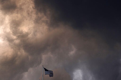 FILE - In this March 19, 2020, file photo, an American flag is dwarfed by storm clouds as they pass over a downtown Kansas City, Mo. (AP Photo/Charlie Riedel, File)