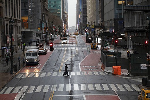 FILE - In this March 23, 2020, file photo, a commuter crosses 42nd Street in front of Grand Central Terminal during morning rush hour, in New York. (AP Photo/Mark Lennihan, File)