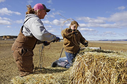 In this March 2, 2020, photo, Erika DuVal and her daughter Helena, 10, prepare to toss hay bales to cattle from the back of a truck at their farm in Tulelake, Calif. DuVal's husband, Ben DuVal, inherited the farm from his grandfather and worries that plan to demolish four dams on the lower Klamath River could set a precedent for dam removal that could eventually threaten his livelihood. The proposal to remove the dams on California's second-largest river to benefit threatened salmon has sharpened a decades-old dispute over who has the biggest claim to the river's life-giving waters. (AP Photo/Gillian Flaccus)