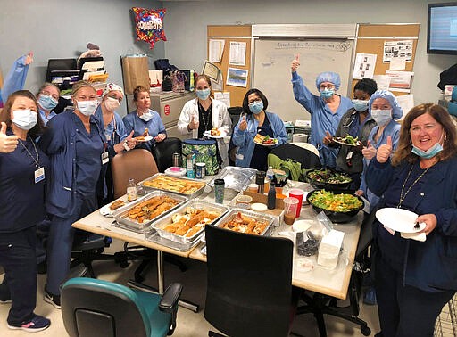 In this March 26, 2020 photo provided by Maureen Morin and Federico's Pizza, staff members of the Hackensack Meridian Jersey Shore University Medical Center give a thumbs-up in Neptune City, N.J., as they eat a donated meal from the Belmar, New Jersey pizzeria. With restaurants closed for all but takeout orders during the coronavirus outbreak, the owners of the pizzeria could have shut down and laid off their 20 employees. Instead, the business's owners took out a $50,000 line of credit and guaranteed their workers they'll stay on the payroll for at least two months. (Courtesy of Maureen Morin via AP)