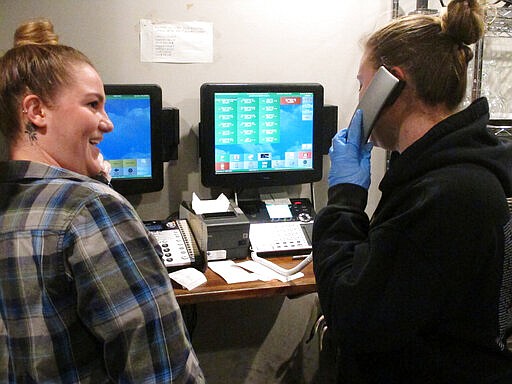 In this March 24, 2020 photo, Kirsten Phillips, left, and Sylvia Pappa, right, take telephone orders at Federico's Pizza in Belmar N.J. The owners of the business took out a $50,000 line of credit to ensure that their employees can stay on the payroll for at least two months during the virus outbreak. That prompted an outpouring of donations from customers wanting to send pizzas to hospital workers and first responders. (AP Photo/Wayne Parry)