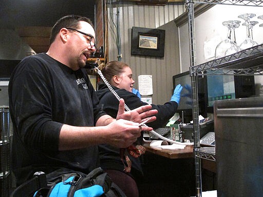 In this March 24, 2020 photo, Michael Morin, left, and Sylvia Pappa, right, take telephone orders at Federico's Pizza in Belmar N.J. The owners of the business took out a $50,000 line of credit to ensure that their employees can stay on the payroll for at least two months during the virus outbreak. That prompted an outpouring of donations from customers wanting to send pizzas to hospital workers and first responders. (AP Photo/Wayne Parry)