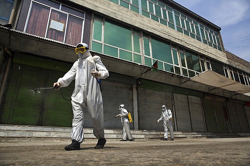 Volunteers in protective suits spray disinfectant on storefronts to help curb the spread of the coronavirus in Kabul, Afghanistan, Sunday, March 29, 2020. The government Friday ordered a three-week lock-down for Kabul to stem the spread of the new coronavirus. (AP Photo/Rahmat Gul)