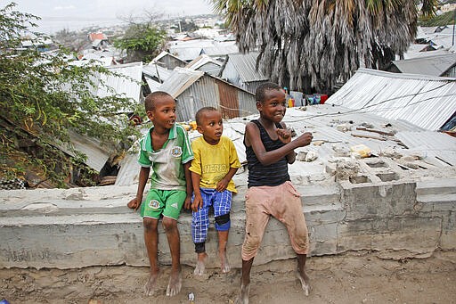 In this photo taken Thursday, March 26, 2020, children sit on a wall overlooking densely packed houses in the Sayidka camp for internally displaced people in Mogadishu, Somalia. The country has only a handful of confirmed cases of the new coronavirus so far but residents of the camp, who have already fled drought and violence from the Islamist al-Shabab militant group, say they are fearful of the virus and feel vulnerable. (AP Photo/Farah Abdi Warsameh)