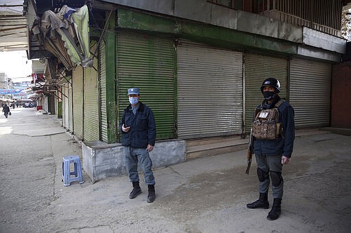 Police officers guard shuttered storefronts following a lockdown amid concern over spread of coronavirus in Kabul, Afghanistan, Sunday, March 29, 2020. The Afghan government Friday ordered a three-week lock-down for Kabul to stem the spread of the virus. (AP Photo/Rahmat Gul)