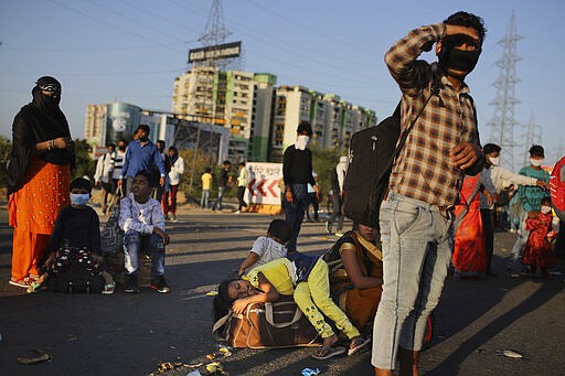 A young girl lies on a luggage as she along with her family awaits transportation to her village following a lockdown amid concern over spread of coronavirus in New Delhi, India, Saturday, March 28, 2020. Authorities sent a fleet of buses to the outskirts of India's capital on Saturday to meet an exodus of migrant workers desperately trying to reach their home villages during the world's largest coronavirus lockdown. Thousands of people, mostly young male day laborers but also families, fled their New Delhi homes after Prime Minister Narendra Modi announced a 21-day lockdown that began on Wednesday and effectively put millions of Indians who live off daily earnings out of work. (AP Photo/Altaf Qadri)