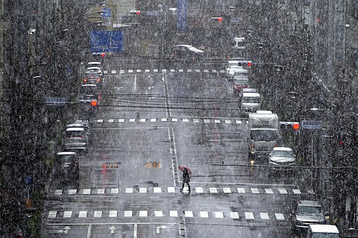 A woman walks in falling snow in Tokyo Saturday, March 28, 2020. Tokyo Gov. Yuriko Koike has repeatedly asked the city's 13 million residents to stay home this weekend, saying the capital is on the brink of an explosion in virus infections. She warned of a possible hard shutdown of the city if the spread of the virus doesn't slow. (AP Photo/Eugene Hoshiko)