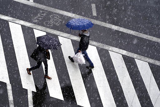 Men walk in falling snow in Tokyo Saturday, March 28, 2020. Tokyo Gov. Yuriko Koike has repeatedly asked the city's 13 million residents to stay home this weekend, saying the capital is on the brink of an explosion in virus infections. She warned of a possible hard shutdown of the city if the spread of the virus doesn't slow. (AP Photo/Eugene Hoshiko)