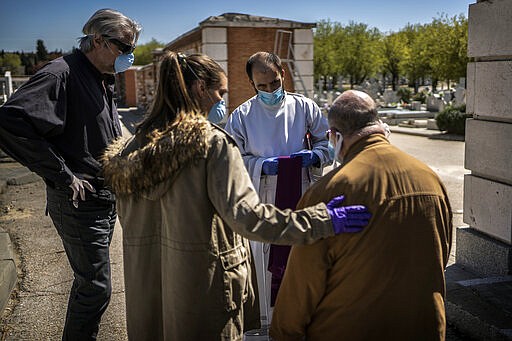 From left to right, the son-in-law, daughter and husband, no names available, of an elderly victim of the COVID-19 talk to the priest before the burial at the Almudena cemetery in Madrid, Spain, Saturday March 28, 2020. In Spain, where stay-at-home restrictions have been in place for nearly two weeks, the official number of deaths is increasing daily. The new coronavirus causes mild or moderate symptoms for most people, but for some, especially older adults and people with existing health problems, it can cause more severe illness or death. (AP Photo/Olmo Calvo)