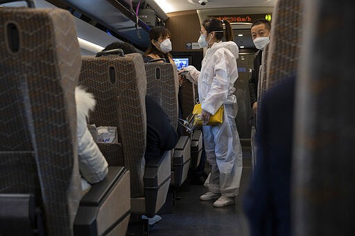 A traveler wearing a protective suit chats with another onboard a train leaving from the train station in Beijing on Sunday, March 29, 2020. As the coronavirus epicenter has shifted westward, the situation has calmed in China, with falling death rates and most new cases coming from abroad, restrictions on travel have been slowly lifted. (AP Photo/Ng Han Guan)