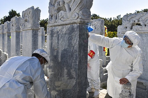 In this Saturday, March 28, 2020, photo released by Xinhua News Agency, cemetery workers in protective suits clean tombs at the Babaoshan cemetery in Beijing. People can ask the cemetery to help clean up the tombs and place flowers and offerings to their deceased relatives during the Qingming Festival, which falls on April 4 this year, to prevent the normally large family gatherings following the new coronavirus outbreak. (Peng Ziyang/Xinhua via AP)