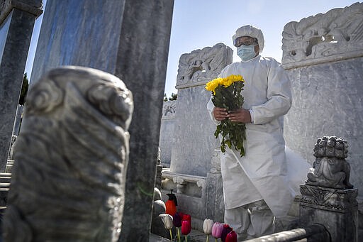 In this Saturday, March 28, 2020, photo released by Xinhua News Agency, a cemetery worker in a protective suit makes an offering of flowers at a grave site in the Babaoshan cemetery in Beijing. People can ask the cemetery to help clean up the tombs and place flowers and offerings to their deceased relatives during the Qingming Festival, which falls on April 4 this year, to prevent the normally large family gatherings following the new coronavirus outbreak. (Peng Ziyang/Xinhua via AP)