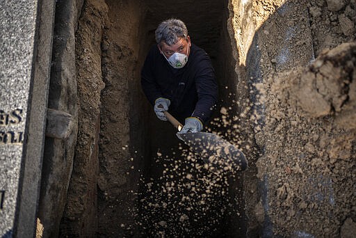 An undertaker prepares a grave for the burial of a victim of the COVID-19 at the Almudena cemetery in Madrid, Spain, Saturday March 28, 2020. In Spain, where stay-at-home restrictions have been in place for nearly two weeks, the official number of deaths is increasing daily. The new coronavirus causes mild or moderate symptoms for most people, but for some, especially older adults and people with existing health problems, it can cause more severe illness or death. (AP Photo/Olmo Calvo)