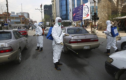 Volunteers in protective suits spray disinfectant on passing vehicles helping curb the spread of the coronavirus in Kabul, Afghanistan, Sunday, March 29, 2020. The government Friday ordered a three-week lock-down for Kabul to stem the spread of the new coronavirus. (AP Photo/Rahmat Gul)