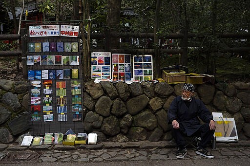 Artist Kinji Kimura, 76, who sells postcard-sized prints of work, sits on a stool while waiting for customers near the Arashiyama Bamboo Forest in Kyoto, Japan, March 18, 2020. &quot;Arashiyama is empty,&quot; is a new catchphrase that appeared on posters in the area. &quot;It's time to visit Kyoto,&quot; they say, because there are no long lines and waiting to do river rafting, get into popular temples or cross the bridge. (AP Photo/Jae C. Hong)