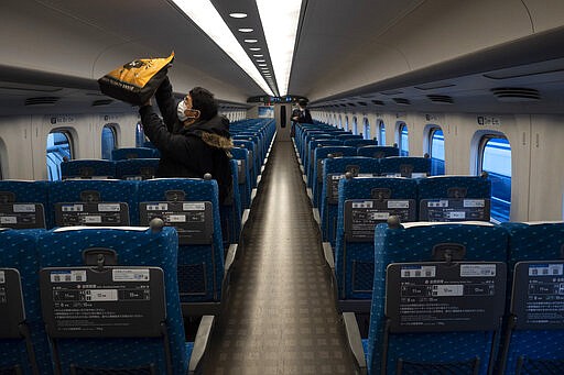 A traveler places his bag in an overhead luggage rack in a bullet train bound for Kyoto and Osaka at Tokyo Station in Tokyo, March 17, 2020. (AP Photo/Jae C. Hong)