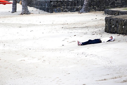 A man rests on Waikiki Beach in Honolulu on Saturday, March 28, 2020. Like many cities across the world, Honolulu came to an eerie standstill this weekend as the coronavirus pandemic spread throughout the islands. But Hawaii officials went beyond the standard stay-at-home orders and effectively flipped the switch on the state's tourism-fueled economic engine in a bid to slow the spread of the virus. As of Thursday, anyone arriving in Hawaii must undergo a mandatory 14-day self-quarantine. The unprecedented move dramatically reduced the number of people on beaches, in city parks and on country roads where many people rely on tourism to pay for the high cost of living in Hawaii. (AP Photo/Caleb Jones)