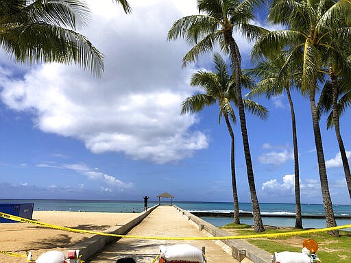 A man walks along a closed pier on Waikiki Beach in Honolulu on Saturday, March 28, 2020. Like many cities across the world, Honolulu came to an eerie standstill this weekend as the coronavirus pandemic spread throughout the islands. But Hawaii officials went beyond the standard stay-at-home orders and effectively flipped the switch on the state's tourism-fueled economic engine in a bid to slow the spread of the virus. As of Thursday, anyone arriving in Hawaii must undergo a mandatory 14-day self-quarantine. The unprecedented move dramatically reduced the number of people on beaches, in city parks and on country roads where many people rely on tourism to pay for the high cost of living in Hawaii. (AP Photo/Caleb Jones)