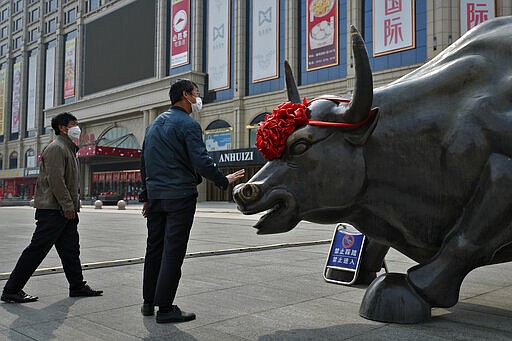 A man wearing a protective face mask touches the investment icon bull statue on display outside a retail and wholesale clothing mall which remain closed following the new coronavirus outbreak in Beijing, Monday, March 30, 2020. Asian shares started the week with fresh losses as countries reported surging numbers of infections from the coronavirus that has prompted shutdowns of travel and business in many parts of the world. (AP Photo/Andy Wong)