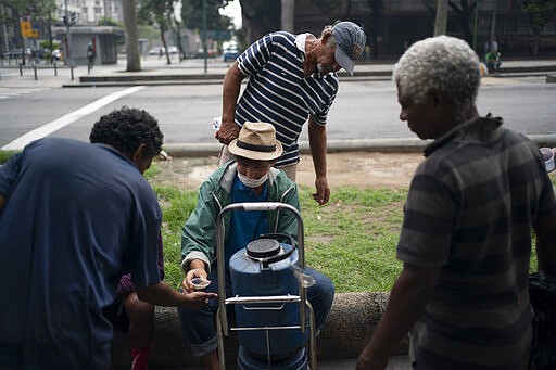 Homeless gather for a free cup of coffee and bread, distributed by Eli Ferreira, center, who started serving free breakfasts to the hungry daily since the outbreak of the new coronavirus, in downtown in Rio de Janeiro, Brazil, Monday, March 30, 2020. Ferreira, who used to serve food twice a week before the outbreak, said he knows he is breaking the rules of social distancing but that &quot;what counts now is the human side.&quot; (AP Photo/Leo Correa)