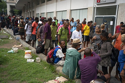 Homeless gather for a free cup of coffee and bread, distributed by Eli Ferreira, wearing hat, who started serving free breakfast to the hungry daily since the outbreak of the new coronavirus, in downtown in Rio de Janeiro, Brazil, Monday, March 30, 2020. Ferreira, who used to serve food twice a week before the outbreak, said he knows he is breaking the rules of social distancing but that &quot;what counts now is the human side.&quot; (AP Photo/Leo Correa)