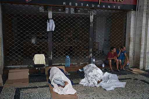 Homeless sleep on the sidewalk outside a closed restaurant in downtown Rio de Janeiro, Brazil, Monday, March 30, 2020, while most other residents stay inside indoors to help contain the spread of the new coronavirus. (AP Photo/Leo Correa)