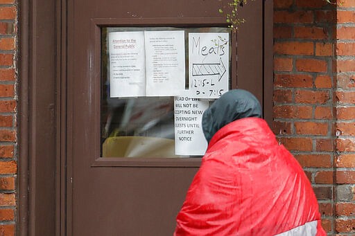 A man carrying a sleeping bag looks at a sign on the door of the Bread of Life Mission in Seattle's downtown Pioneer Square neighborhood that says the facility will not be accepting new overnight guests, Monday, March 30, 2020 in Seattle. On Saturday, March 28, 2020, public health officials in King County announced the first positive new coronavirus cases among the county's homeless population, (AP Photo/Ted S. Warren)