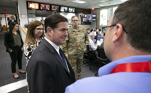 FILE - In this March 18, 2020, file photo, Arizona Gov. Doug Ducey, foreground left, talks to Matt Heckard, right, assistant director of preparedness with the state's Department of Emergency and Military Affairs, as members of DEMA work responding to the coronavirus pandemic, in the DEMA operations center at the Arizona National Guard Papago Park Military Reservation in Phoenix. Maj. Gen. Michael T. McGuire, background center, the director of DEMA, and Wendy Smith-Reeve, stand next to Ducey. Smith-Reeve, director of the Arizona Division of Emergency Management, submitted her resignation Saturday, March 29. The state's emergency operations will now be directed by Maj. Gen. Michael T. McGuire. (David Wallace/The Arizona Republic via AP, Pool, File)