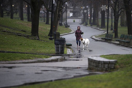 A passer-by walks a dog Sunday, March 29, 2020, along a path in the Boston Common, in Boston. Many people are working from home while many businesses have closed indefinitely because of the coronavirus, leaving portions of the city nearly empty. The new coronavirus causes mild or moderate symptoms for most people, but for some, especially older adults and people with existing health problems, it can cause more severe illness or death. (AP Photo/Steven Senne)