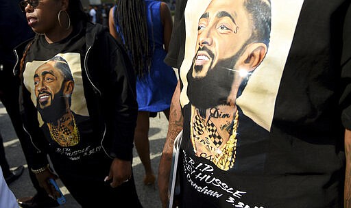 FILE - In this April 11, 2019 file photo, mourners wear T-shirts in tribute to Nipsey Hussle at a memorial service for the rapper at the Staples Center in Los Angeles. Hussle, 33, was shot and killed outside his Los Angeles clothing store on March 31, 2019. A year after Hussle's death, his popularity and influence are as strong as ever. He won two posthumous Grammys in January, he remains a favorite of his hip-hop peers and his death has reshaped his hometown of Los Angeles in some unexpected ways. (Photo by Chris Pizzello/Invision/AP, File)