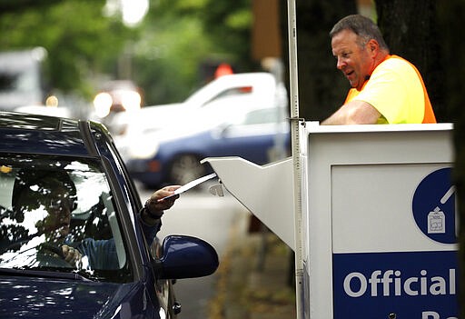 FILE - In this May 16, 2016, file photo election worker Randy Polivka watches as a motorist drops off their ballot at a ballot drop box site in Portland, Ore. The coronavirus has knocked presidential primaries back several weeks as officials worry about voters crowding into polling places. If the disease remains a hazard in November, Democrats say there's only one solution to preserve the November election, national voting by mail. (AP Photo/Don Ryan, File)