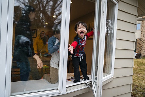 In this Wednesday, March 25, 2020, photo, Parker Royce, 4, feels raindrops while reaching out the ground floor window of his home in Roseville, Minn. Andrea Royce spent time homeschooling her three children with help from a friend that helps with childcare. (Leila Navidi/Star Tribune via AP)