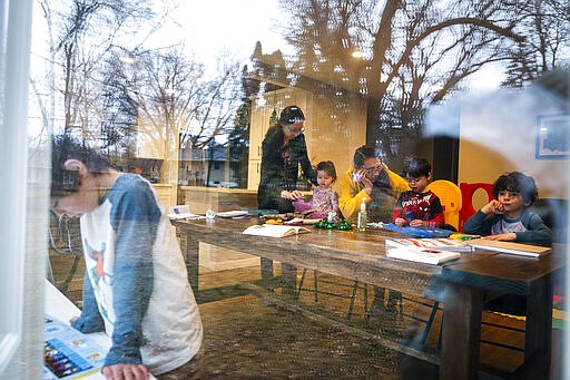 In this Wednesday, March 25, 2020, photo, Andrea Royce, standing at center, homeschools her children Rowan, from left, 6, Lucy, 1, and Parker, 4, with the help of friend Carlota Bernal, third from right, who helps with childcare, with her son Blaze Boxell, far right, in Roseville, Minn. Parents are taking on the role of educators now that the schools are closed due to the new coronavirus pandemic. (Leila Navidi/Star Tribune via AP)