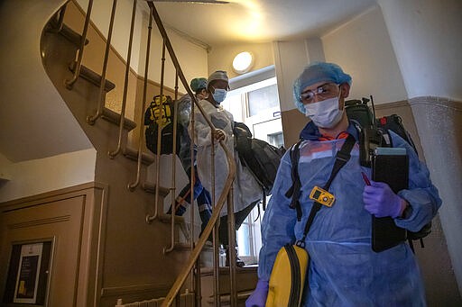 In this photo taken Saturday March 28 2020, members of the Civil Protection service, Noemie Biamba, left, and Cyril Lamriben, right, escort a 51-year-old woman, possibly infected with the coronavirus infection, from her flat to an ambulance in Paris. (AP Photo/Michel Euler)