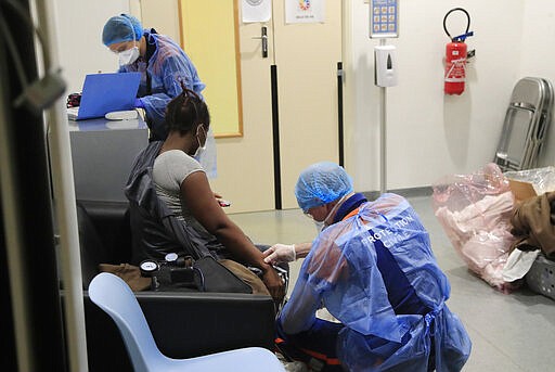 In this photo taken Thursday, March 26, 2020, Vincent Jactel, a member of the Civil Protection service, checks the pulse of a 27-year-old pregnant woman suspected of being infected with the Covid-19 virus in a social housing building in Paris. They don't have to put themselves in harm's way, but the volunteers of France's well-known Civil Protection service choose the front line in the fight against the coronavirus. They are often the first to knock on the doors of people calling for help, and who may have the infection or whose confirmed case has taken a downturn. (AP Photo/Michel Euler)