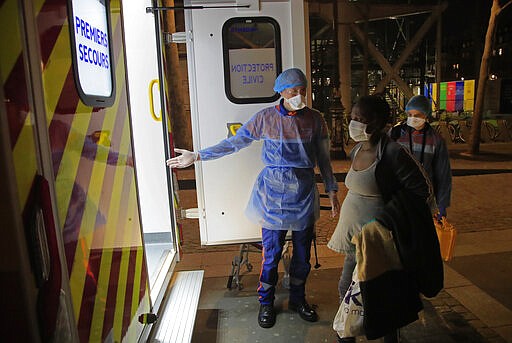 In this photo taken Thursday, March 26, 2020, members of the Civil Protection service, Vincent Jactel, left, and Aurore Lejeune, right, escort a 27-year-old pregnant woman suspected of being infected with the Covid-19 virus in Paris. They don't have to put themselves in harm's way, but the volunteers of France's well-known Civil Protection service choose the front line in the fight against the coronavirus. (AP Photo/Michel Euler)