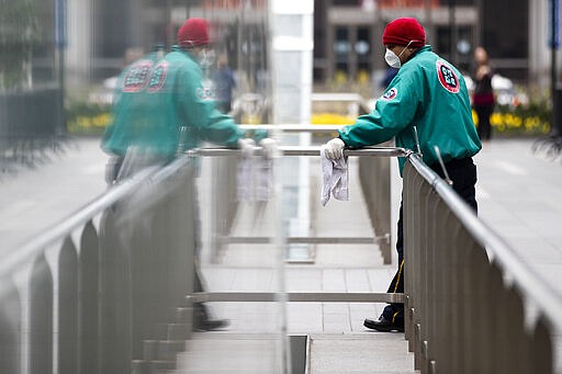 A worker in a protective face mask sanitizes hand rails at the entrances to a train station outside City Hall to help reduce the spread of coronavirus in Philadelphia, Monday, March 30, 2020. (AP Photo/Matt Rourke)