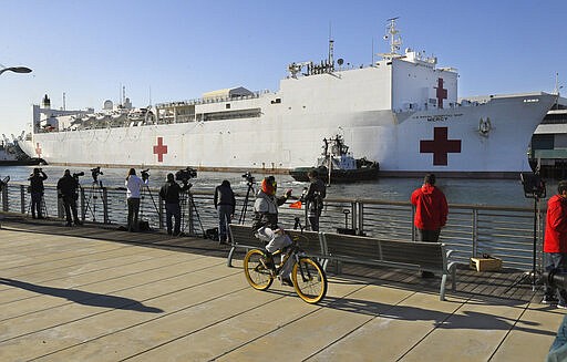 FILE - In this March 27, 2020, file photo, a cyclist rides by the US Naval Ship Mercy enters the Port of Los Angeles. The 1,000-bed USNS Mercy (T-AH 19) docked at the Port of Los Angeles accepted its first patients Sunday, March 29 during its support of the nation's COVID-19 response efforts. The new coronavirus causes mild or moderate symptoms for most people, but for some, especially older adults and people with existing health problems, it can cause more severe illness or death. (AP Photo/Mark J. Terrill, File)