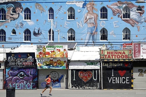 A man jogs in front of closed-off store fronts Sunday, March 29, 2020, in the Venice Beach section of Los Angeles. With cases of coronavirus surging and the death toll increasing, lawmakers are pleading with cooped-up Californians to spend a second weekend at home to slow the spread of the infections. (AP Photo/Marcio Jose Sanchez)